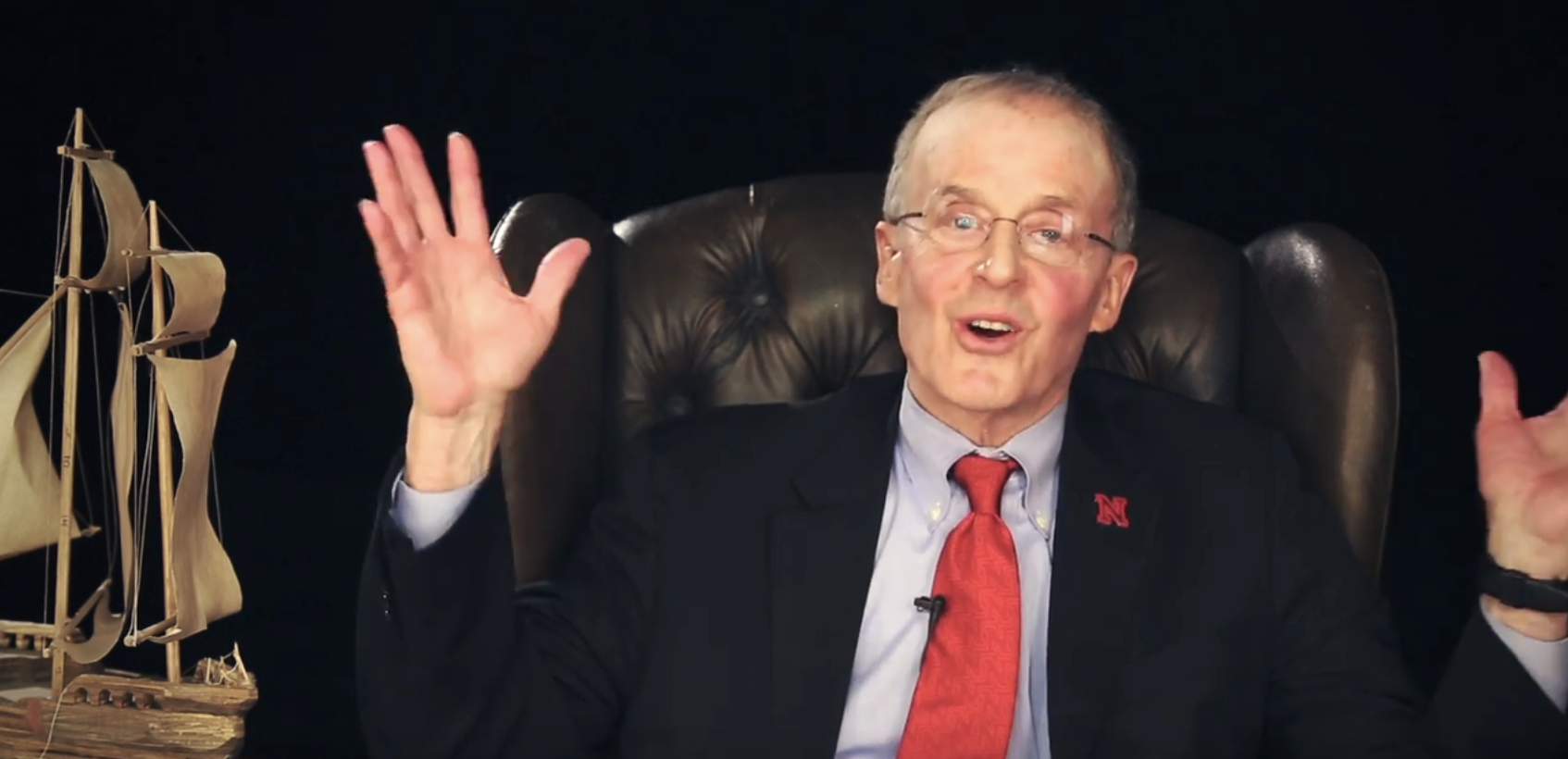Perlman waving his hands in the air excitedly, there is a model wooden ship next to him