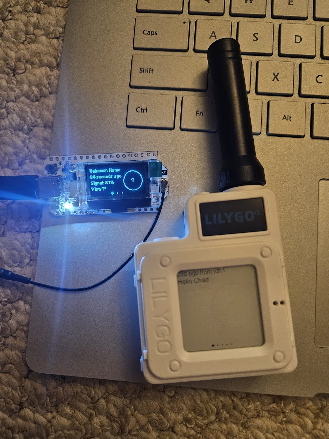 A small board with text on the screen that says 'unknown name 84 seconds ago' and then a LILYGO device next to it with a screen that says 'Hello Chad'